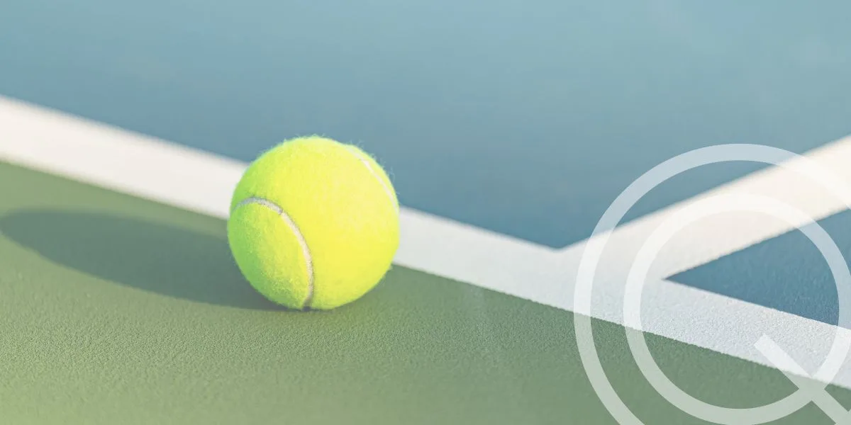 Yellow tennis ball sitting outside the white line of a tennis court